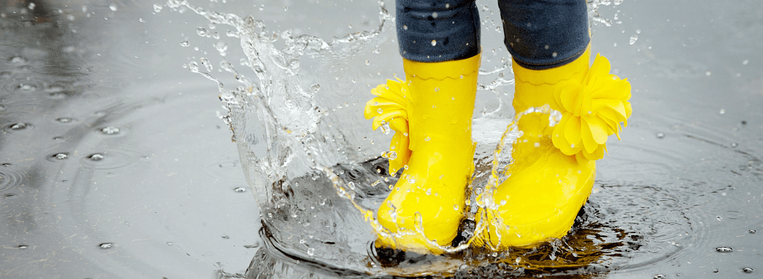 Child wearing yellow rain boots playing in puddle after rain